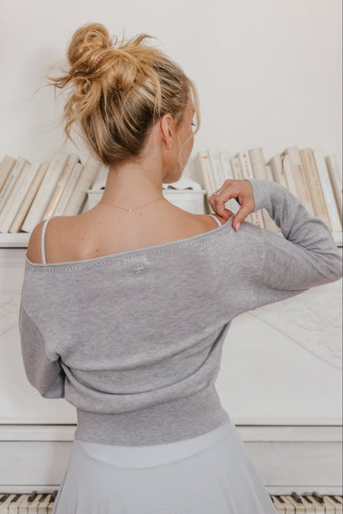 Woman in a Luna Luna gray off-shoulder top and white skirt standing in front of a piano.